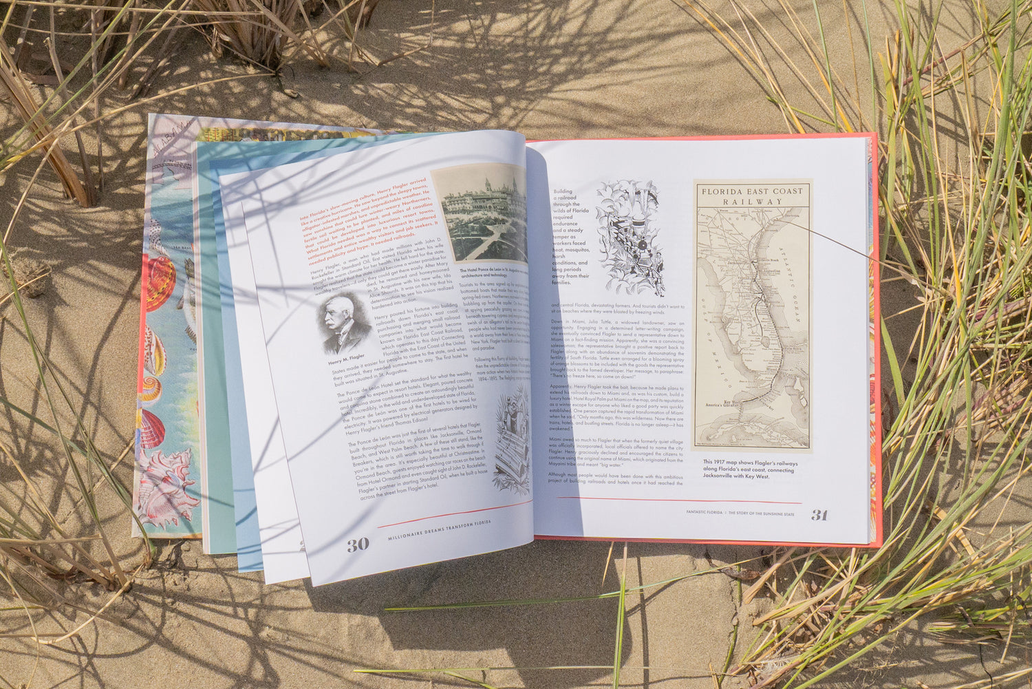 An open book called 'Fantastic Florida' with informational pages laid on sand outdoors, surrounded by beachy grass. The left page has text and a portrait photo, and the right page shows a map and additional text.